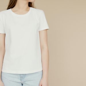 Mockup of a woman in a white t-shirt and jeans on a beige background, ideal for fashion branding.
